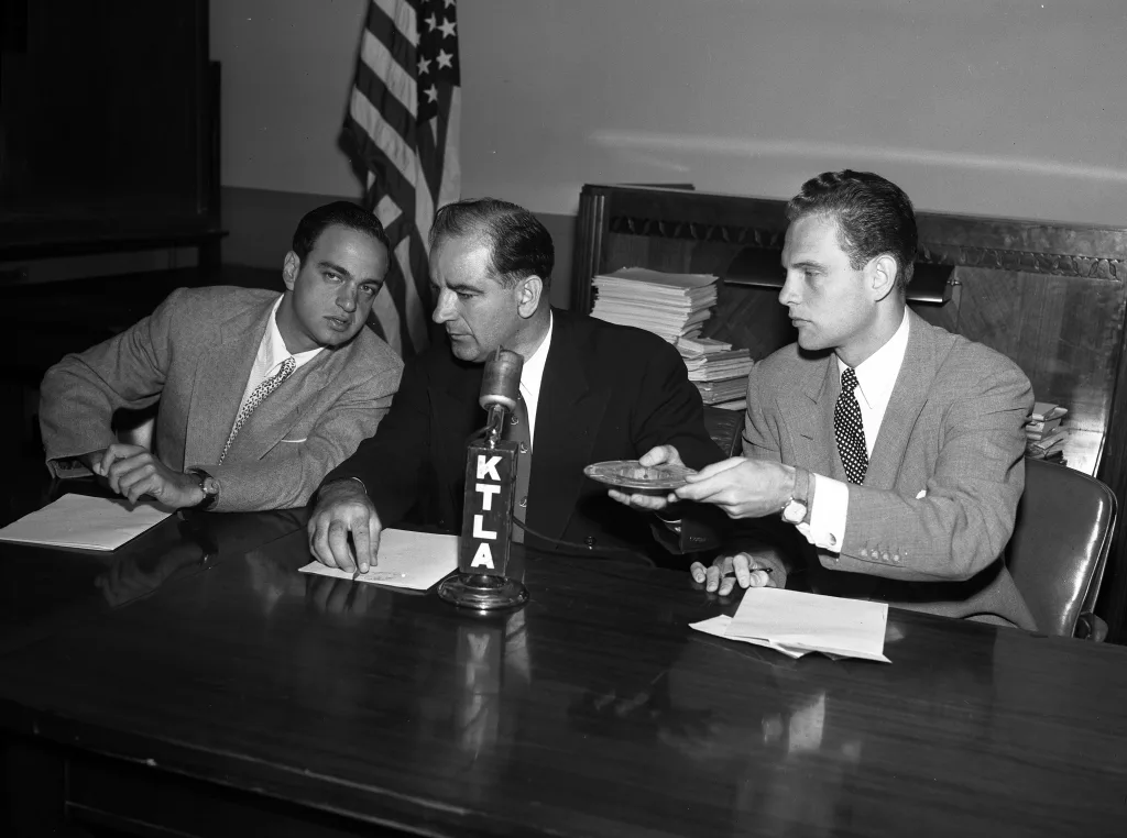 DURING BITTER CLASH - Sen. McCarthy, center, confers with Roy Cohn, chief counsel for House Un-American Activities Committee, during questioning of William Taylor. McCarthy indicated he may seek contempt citation against Taylor. At right is G. David Schine. Uploaded a work by Los Angeles Times from https://digital.library.ucla.edu/catalog/ark:/21198/zz0002shqk. August 23, 1953